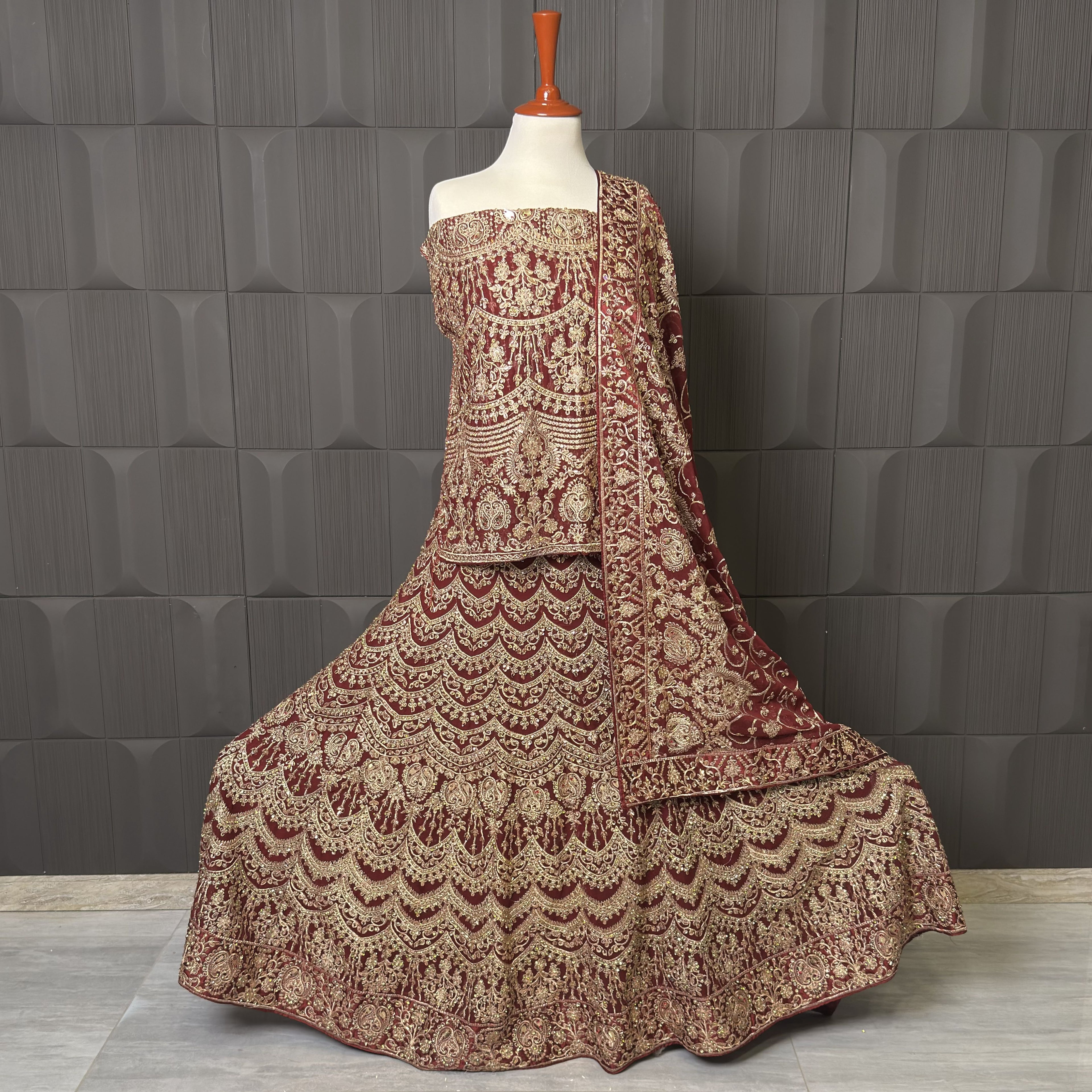 Traditional embroidered outfit on a mannequin against a textured gray wall BRIDAL LEHENGA INDIAN MACHINE WORKI N PAKISTAN PRICE