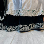 Close-up of a traditional outfit showing a black velvet skirt with intricate silver floral embroidery and green stone embellishments, paired with a white embroidered border.