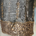 Close-up of a dark gray or black embellished fabric with vertical rows of metallic gold sequins and a wide scalloped gold sequin border at the bottom.