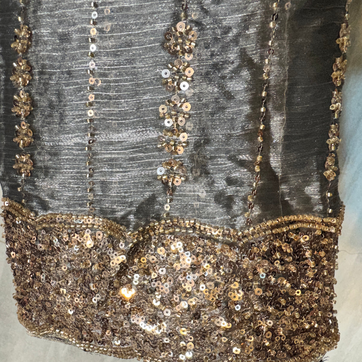 Close-up of a dark gray or black embellished fabric with vertical rows of metallic gold sequins and a wide scalloped gold sequin border at the bottom.
