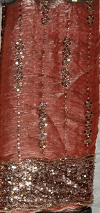 A close-up of a rust-red or terracotta-colored fabric with vertical rows of metallic sequins and a heavily embellished sequined border along the bottom.