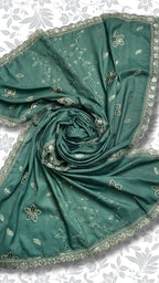 A teal green saree or dupatta with delicate white floral prints and a scalloped embroidered border, styled in a spiral drape against a light gray floral background.