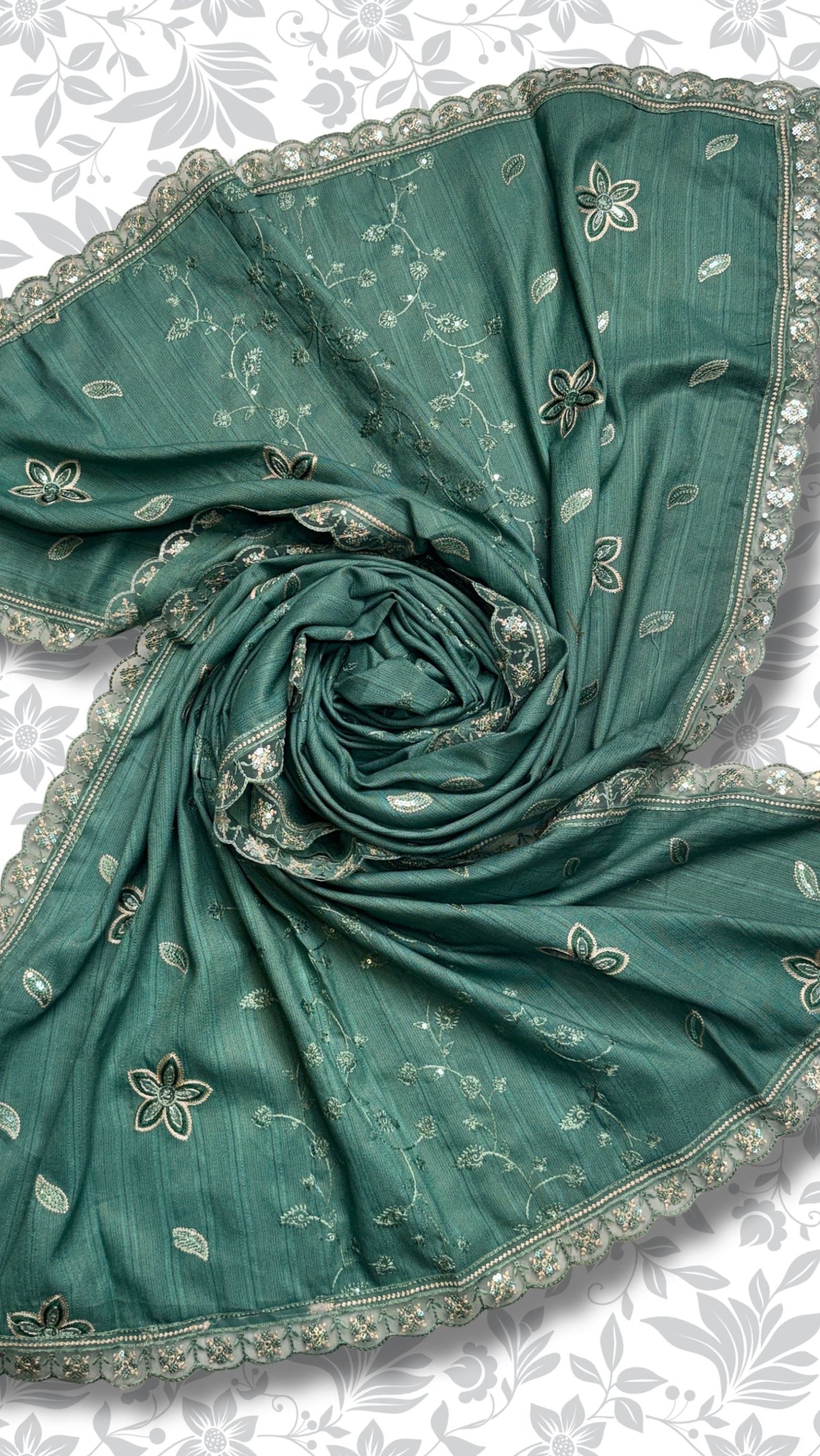 A teal green saree or dupatta with delicate white floral prints and a scalloped embroidered border, styled in a spiral drape against a light gray floral background.