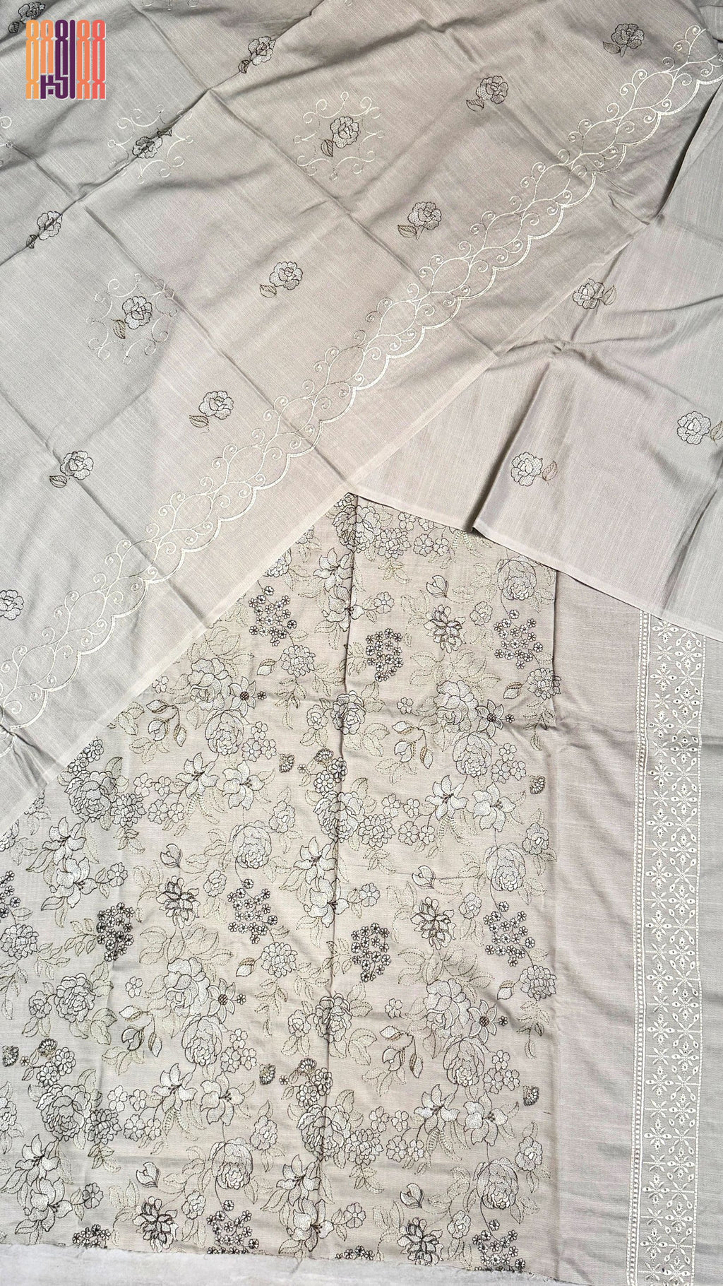 A light beige or off-white fabric garment laid flat, featuring delicate floral embroidery and a decorative border. The fabric has a warm, slightly cream undertone, which maps best to Beige in the allowed color palette.