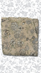 A folded piece of beige fabric with a detailed black and gray floral print, displayed against a white background with a gray floral pattern.