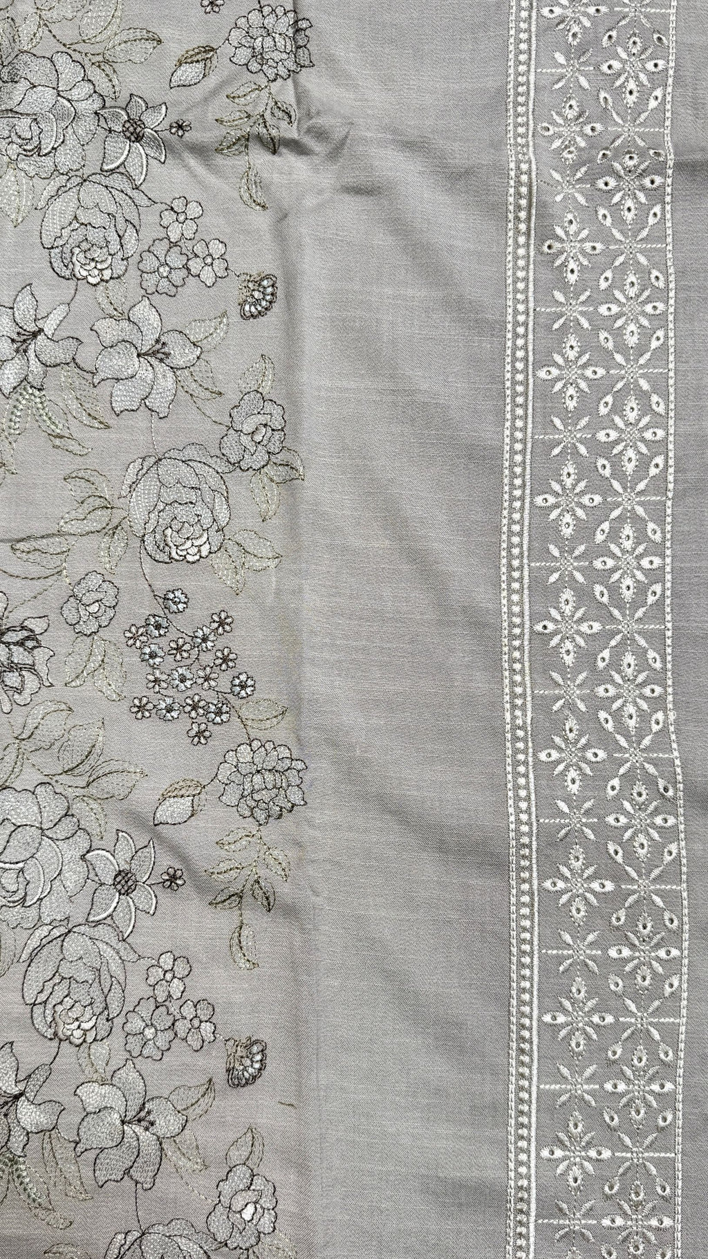 A close-up of a light gray fabric panel with floral embroidery on one side and a decorative embroidered border on the other.