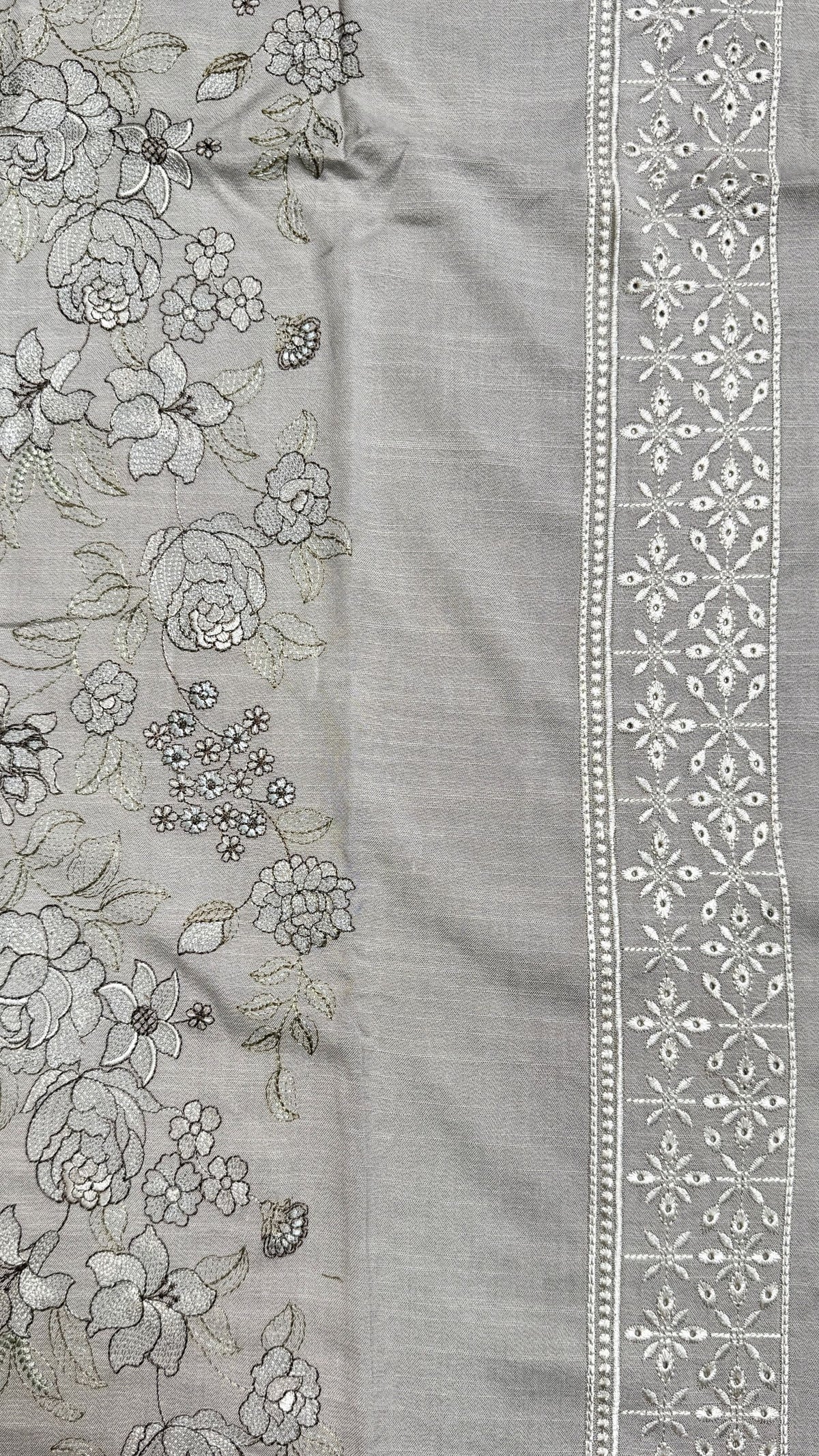 A close-up of a light gray fabric panel with floral embroidery on one side and a decorative embroidered border on the other.