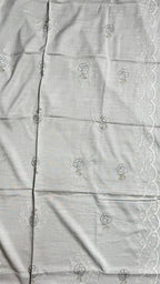 A close-up of a light gray fabric with delicate white floral embroidery and a white scalloped lace border along the right edge.