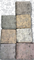 Eight folded fabric pieces with floral line-art patterns are arranged in a grid on a white background with a gray floral watermark. The fabrics come in muted tones including gray, beige, cream, and dusty pink.