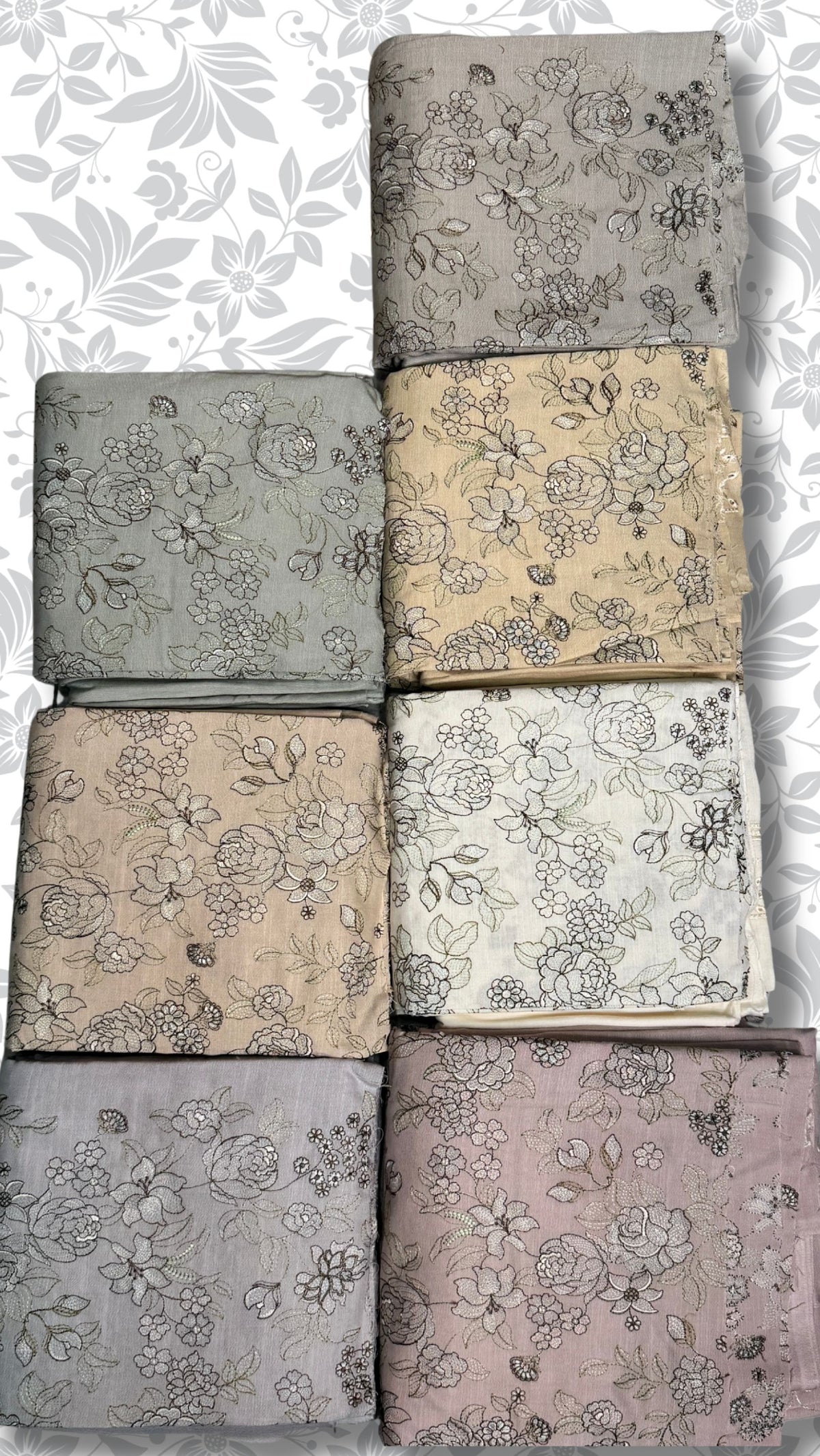 Eight folded fabric pieces with floral line-art patterns are arranged in a grid on a white background with a gray floral watermark. The fabrics come in muted tones including gray, beige, cream, and dusty pink.