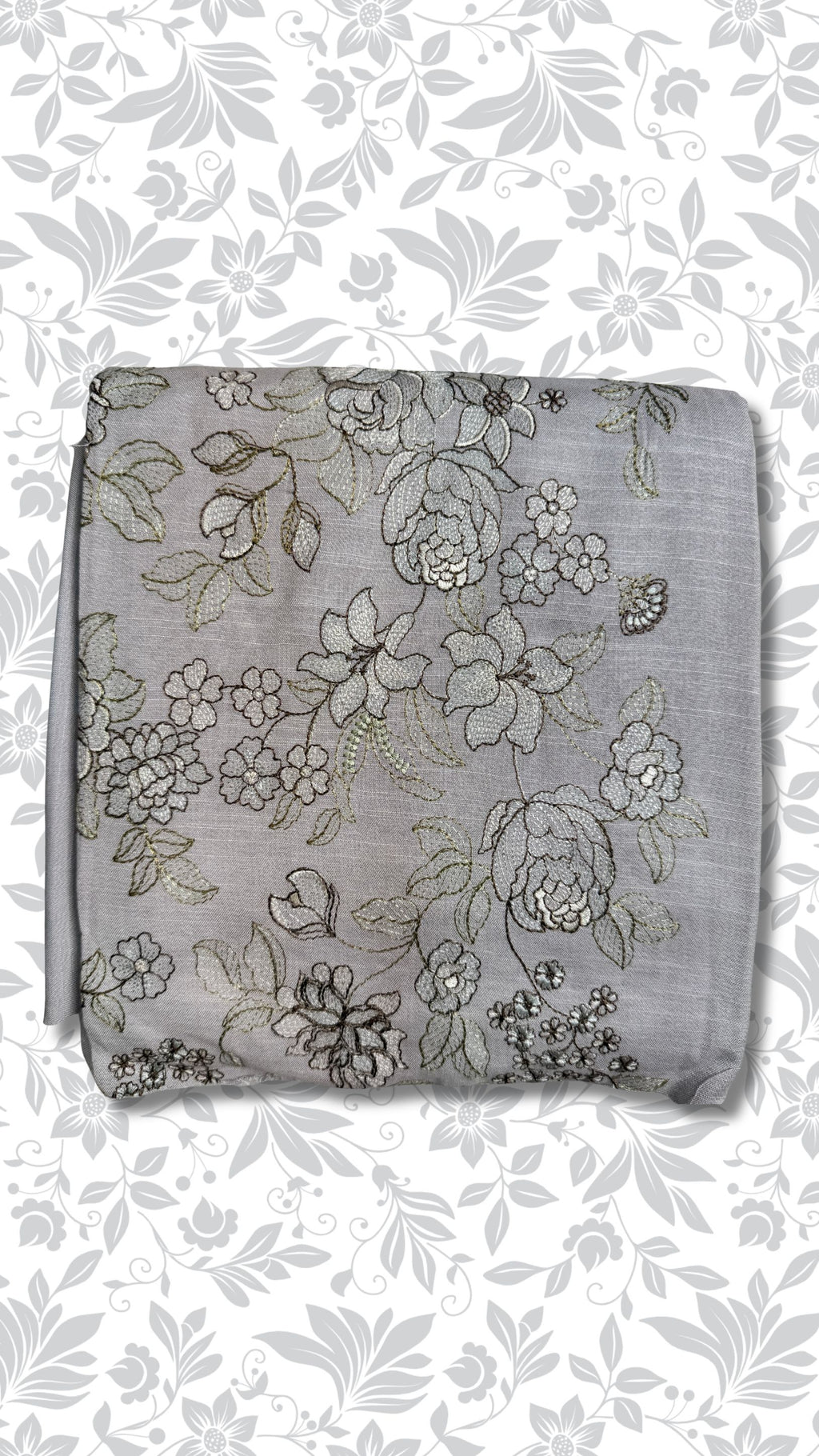 A folded light gray fabric piece with an all-over floral embroidery pattern in gray, black, and subtle gold thread, set against a white background with a gray floral border.