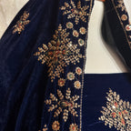 Close-up of a navy blue velvet garment with ornate gold floral embroidery and small red, green, and white embellishments along the neckline and sleeve.