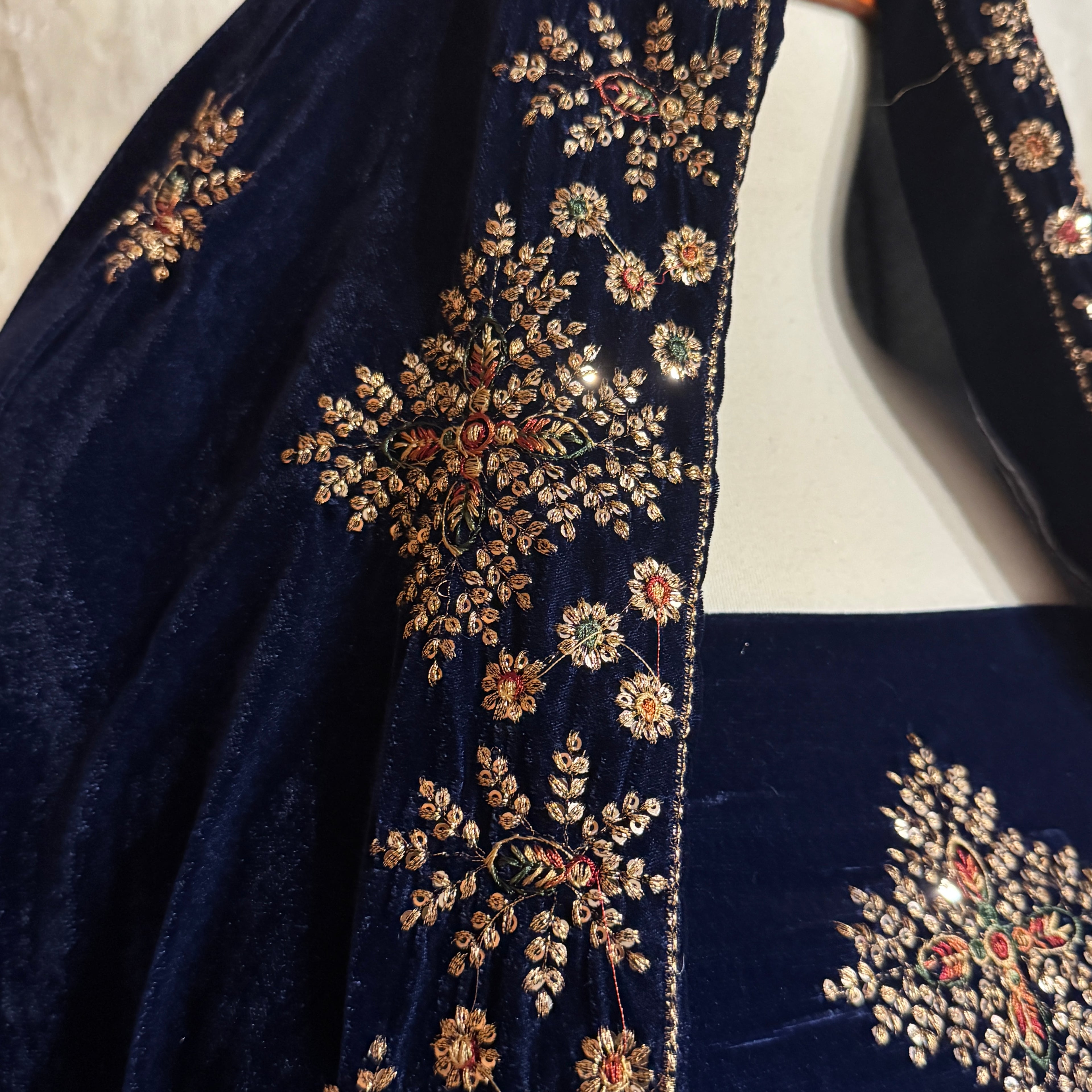 Close-up of a navy blue velvet garment with ornate gold floral embroidery and small red, green, and white embellishments along the neckline and sleeve.