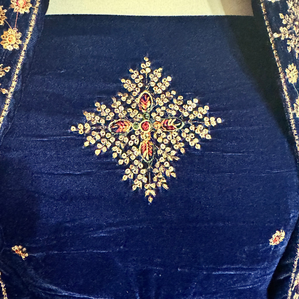 Close-up of a navy blue velvet garment featuring an intricate central floral embroidery with gold, red, and green thread details, and matching embroidered borders on the sides.