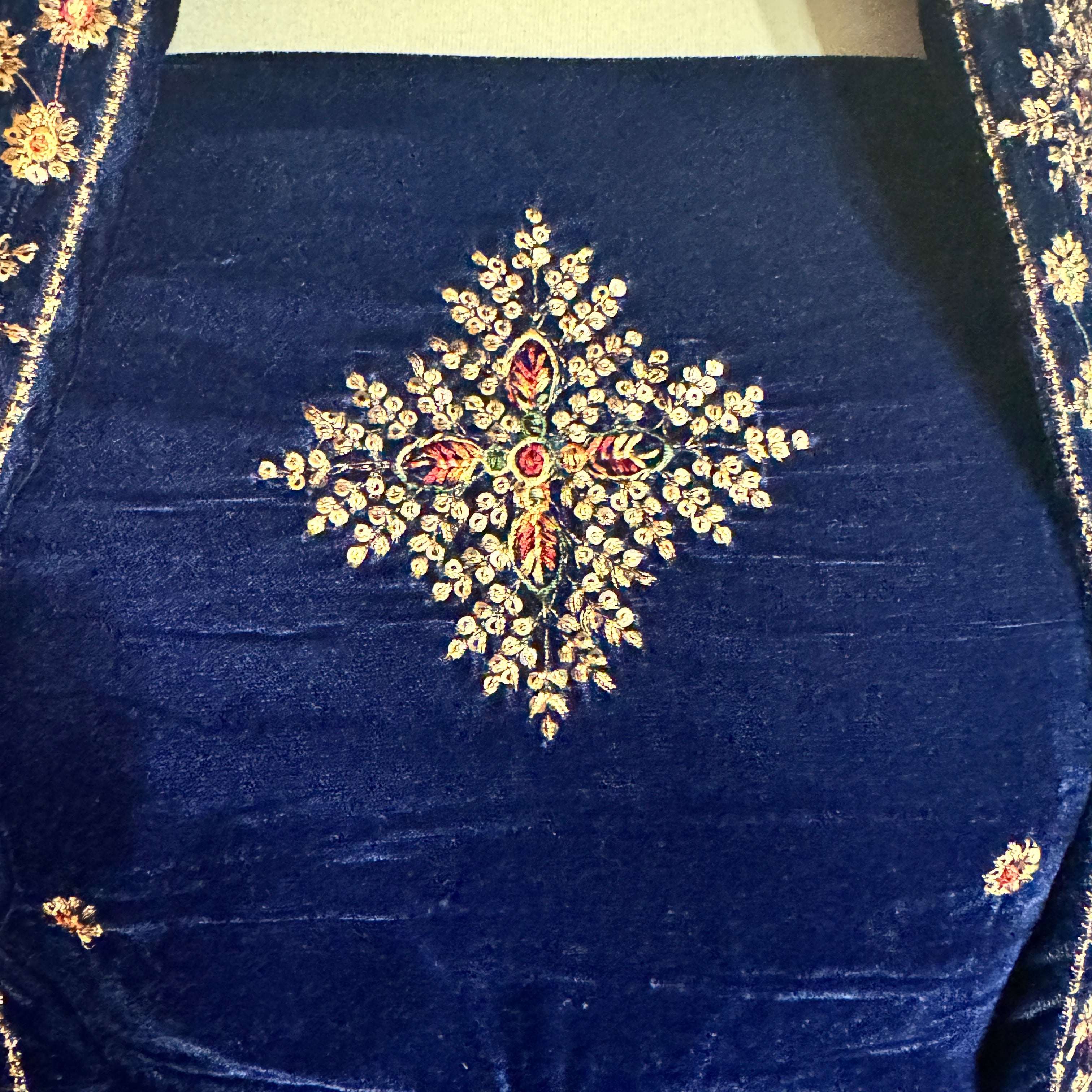 Close-up of a navy blue velvet garment featuring an intricate central floral embroidery with gold, red, and green thread details, and matching embroidered borders on the sides.