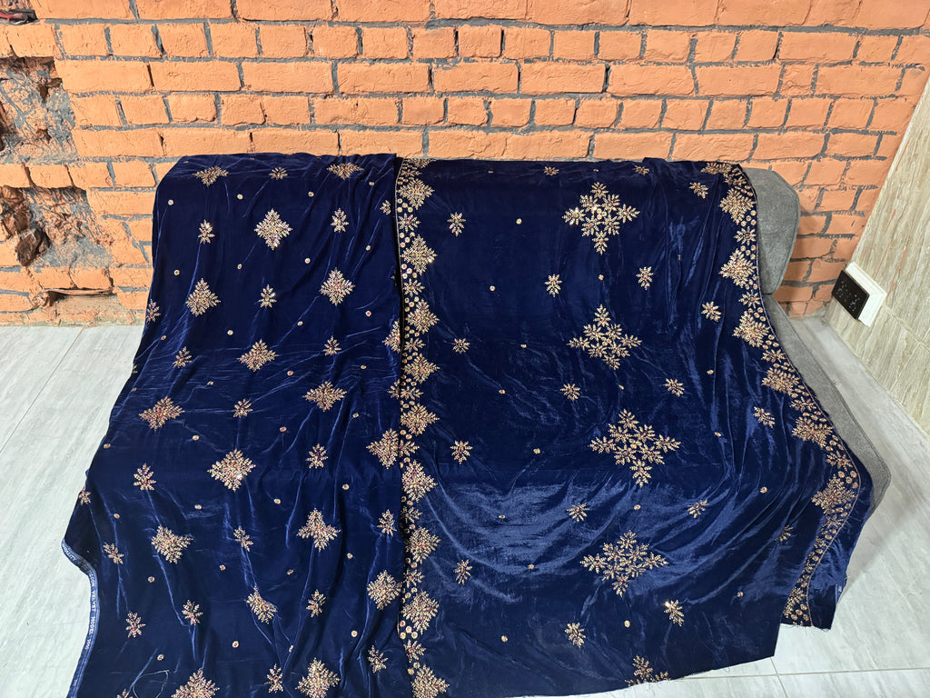 A navy blue velvet throw blanket with gold embroidered snowflake and star patterns draped over a gray sofa in front of a brick wall.