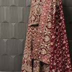 Maroon embroidered fabric with gold patterns against a dark tiled wall INDIAN LEHENGA MACHINE WORK
