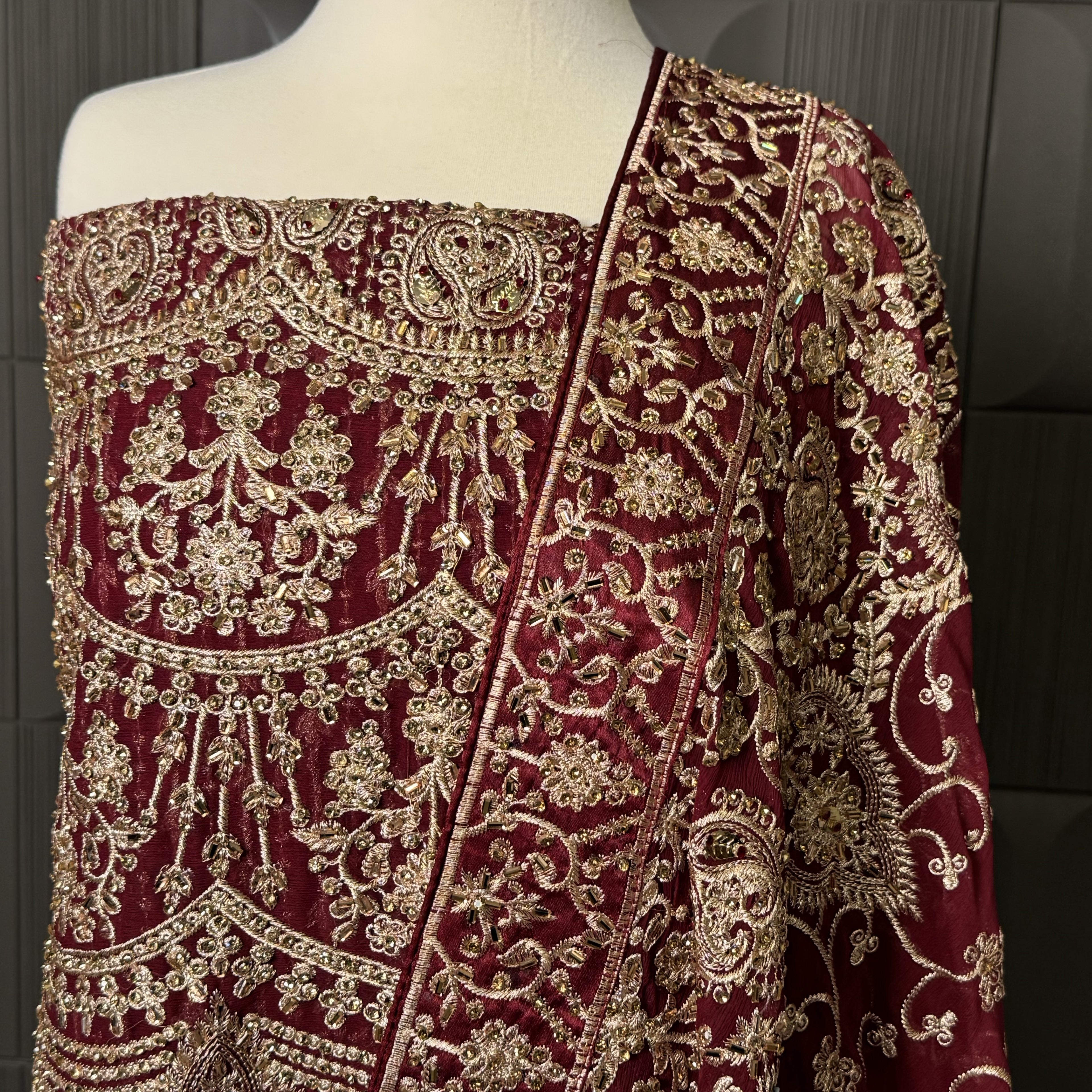 Red fabric with gold embroidery on a mannequin against a dark background