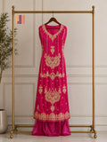 A bright pink traditional dress with intricate gold embroidery displayed on a wooden hanger hanging from a gold clothing rack, set against a light beige paneled wall.