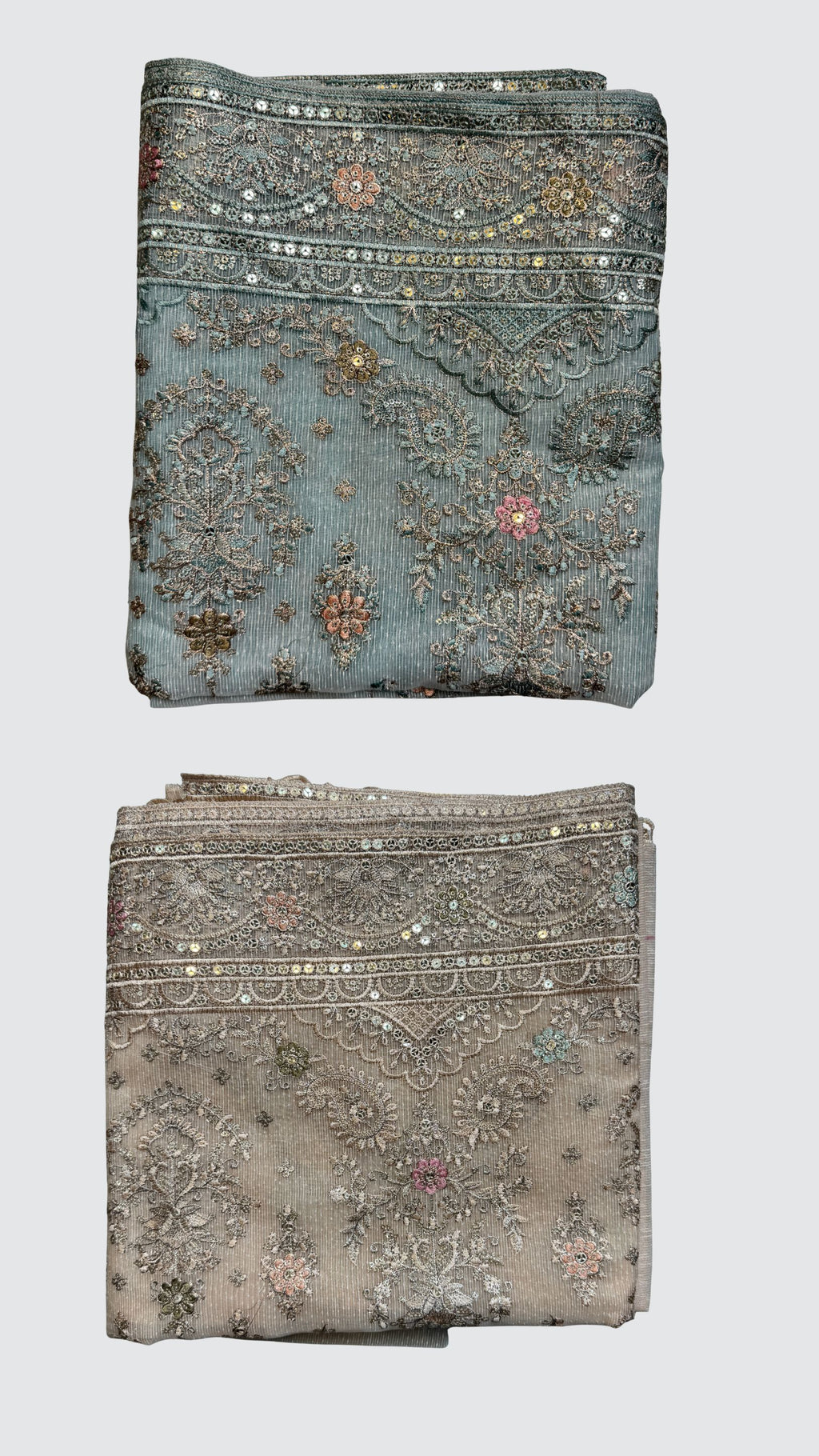 Two folded pieces of ornate embroidered fabric shown vertically on a light gray background. The top piece is dusty blue with silver mirror work and floral embroidery, while the bottom piece is a warm taupe-beige with similar silver embellishment.
