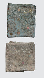 Two folded pieces of ornate embroidered fabric shown vertically on a light gray background. The top piece is dusty blue with silver mirror work and floral embroidery, while the bottom piece is a warm taupe-beige with similar silver embellishment.