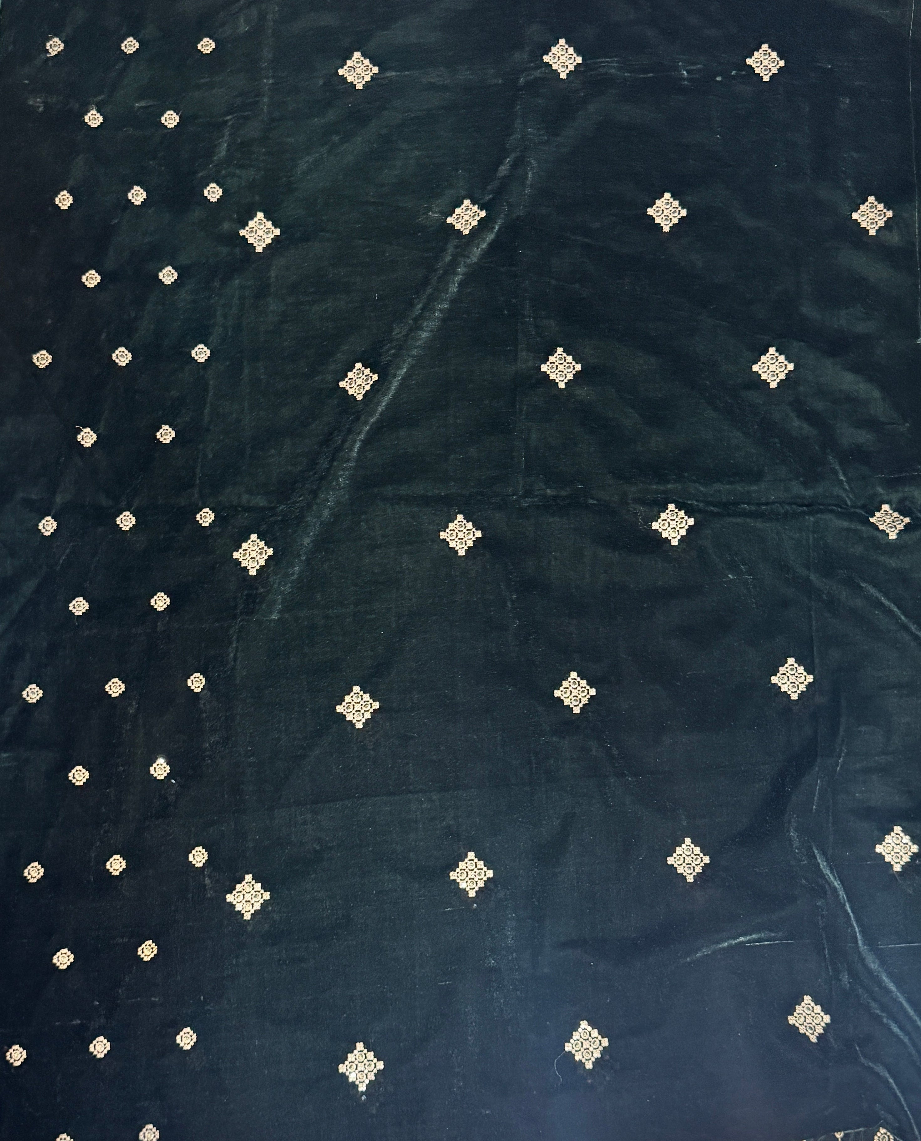 A dark green velvet fabric, likely a saree pallu or dupatta, laid flat on a light-colored tiled floor. The fabric features a border of light green along the edges and is decorated with rows of small, metallic gold diamond-shaped motifs.