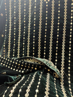 Dark green velvet fabric draped to show its texture and intricate gold zari embroidery, featuring vertical strands of metallic gold beadwork and floral motifs.
