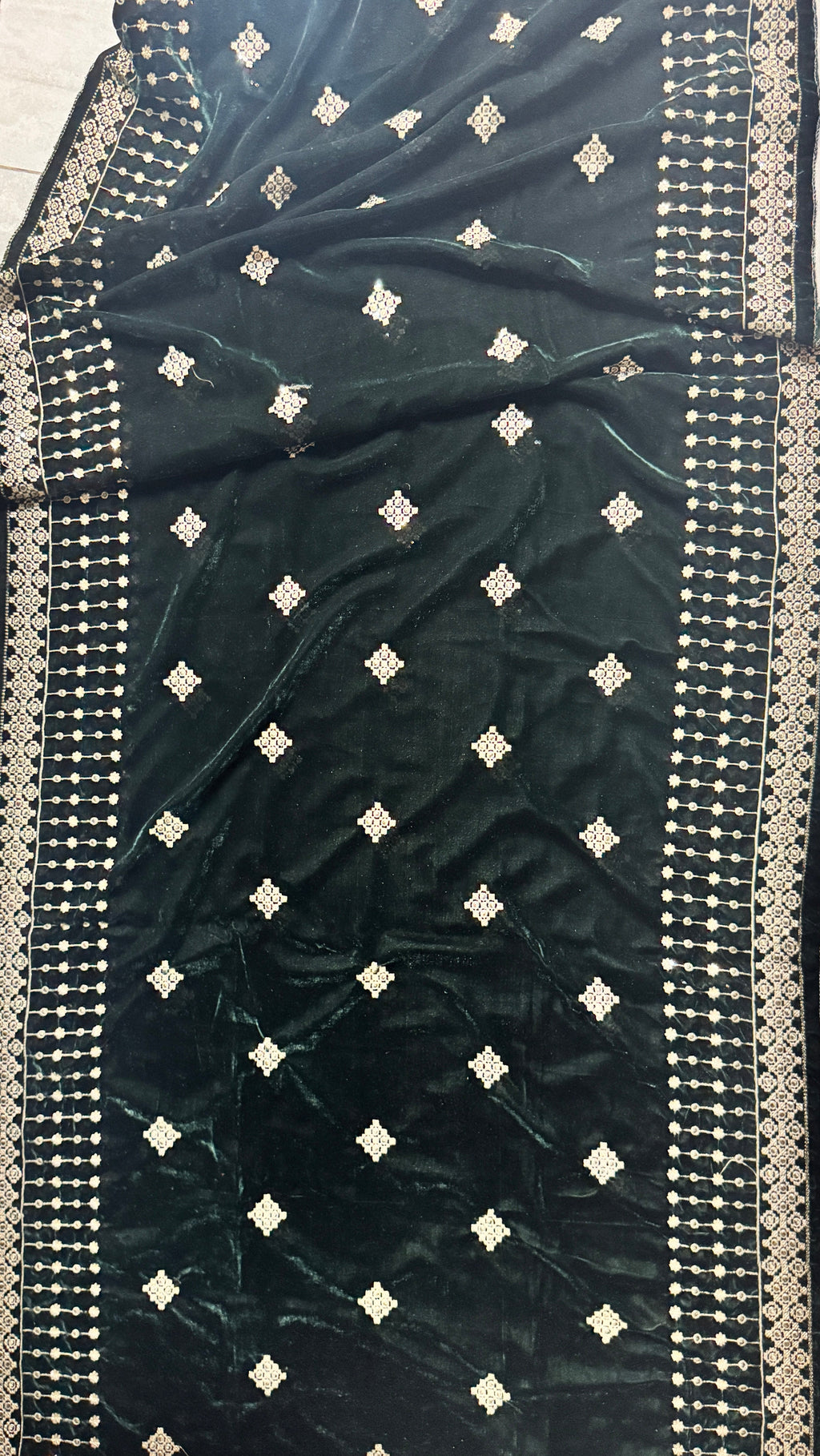 A dark forest green velvet saree or fabric panel with silver embroidered borders and small silver diamond motifs, laid flat on a light-colored floor.