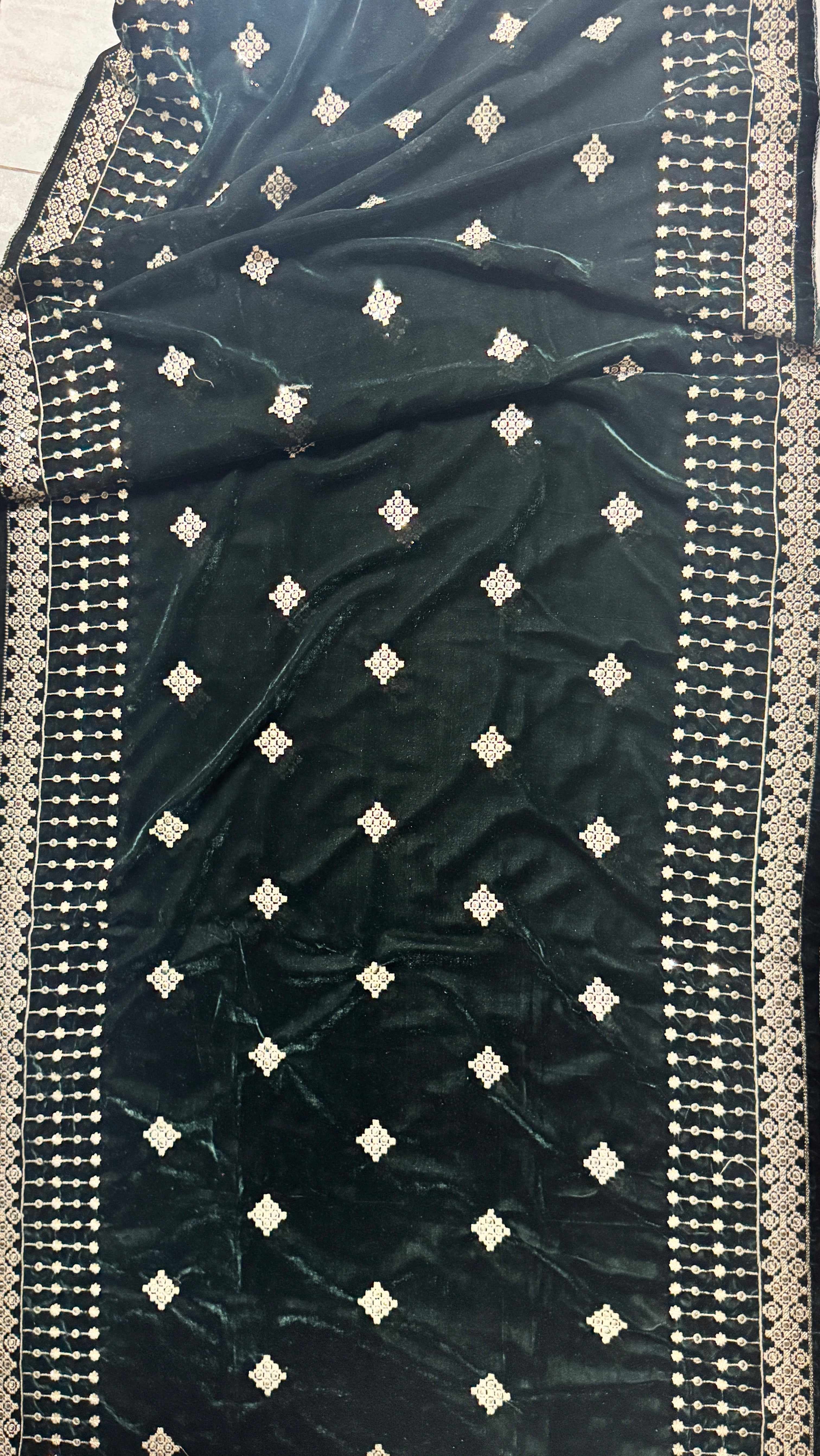 A dark forest green velvet saree or fabric panel with silver embroidered borders and small silver diamond motifs, laid flat on a light-colored floor.