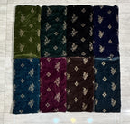 Eight folded fabric samples arranged in a 2x4 grid on a light gray tiled floor. The fabrics come in olive green, forest green, black, navy blue, teal blue, burgundy, brown, and dark teal, each with a small beige floral pattern. Velvet Embroidered Dress 9000