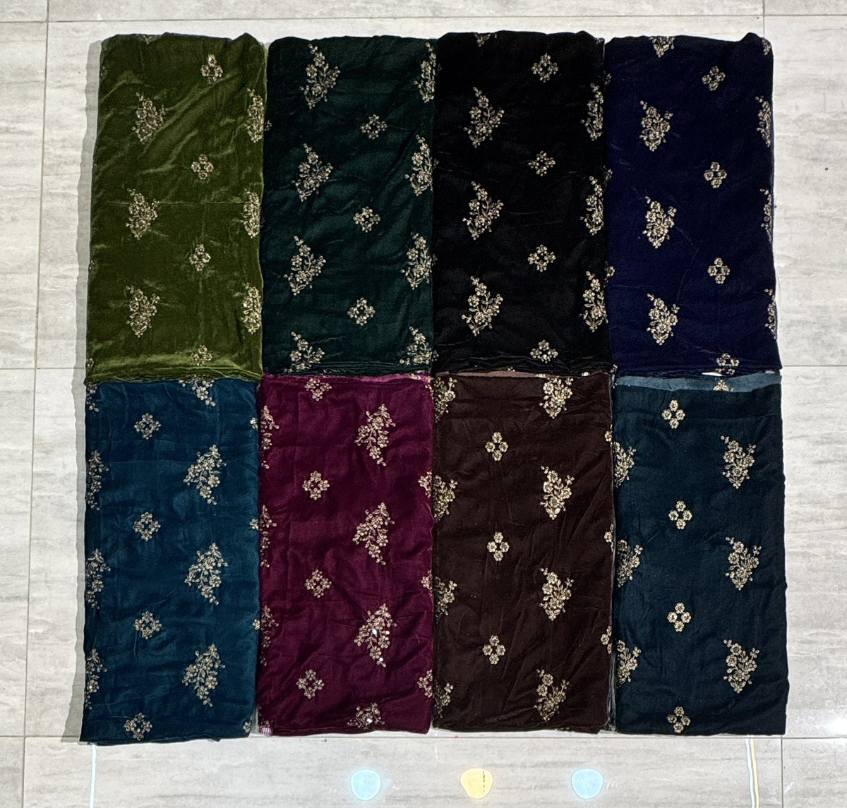 Eight folded fabric samples arranged in a 2x4 grid on a light gray tiled floor. The fabrics come in olive green, forest green, black, navy blue, teal blue, burgundy, brown, and dark teal, each with a small beige floral pattern. Velvet Embroidered Dress 9000